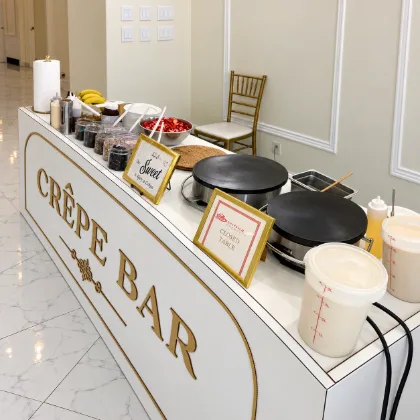 The Crêpe Bar seen from above, with two crepe griddles, a bowl of sliced strawberries, bananas, topping jars and batter containers